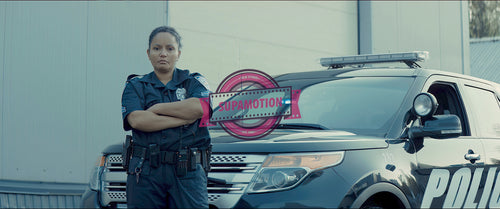 Female police officer posing against police car with flashing lights