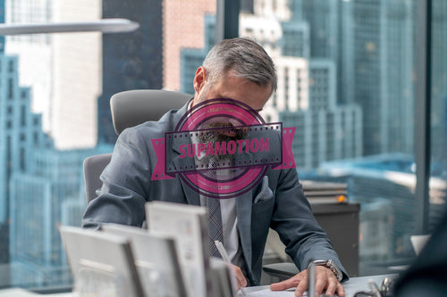 Portrait of 50s adult Caucasian businessman signing documents in his office