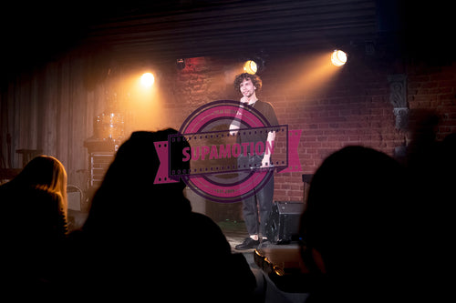 Young Caucasian male comedian performing his stand-up monologue on a stage of a small venue