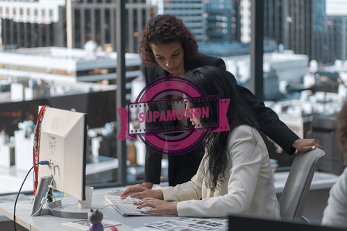 Two diverse female office employees working on something together in the office